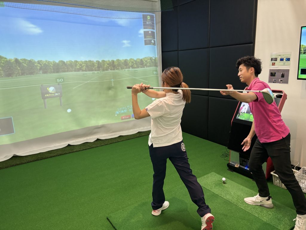 インドアゴルフ施設でレッスンプロからドライバーの指導を受ける女性ゴルファー